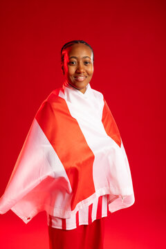 Woman standing and posing in studio with red backdrop, draped in red-and-white flag and skirt