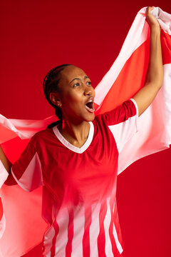 Adult African American woman wearing red-white jersey and studs holding flag shouting in studio
