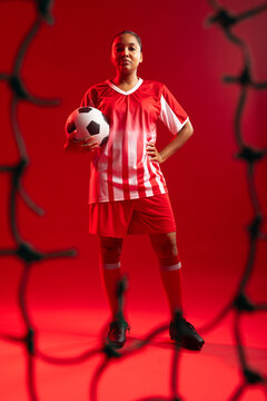 African American female soccer player standing in studio wearing red uniform holding soccer ball