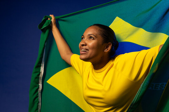 African American woman holding Brazilian flag like cape in yellow shirt, looking upward in studio