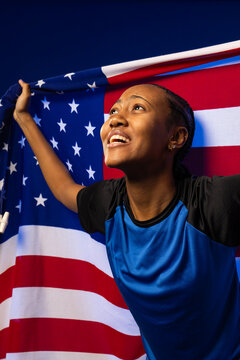 African American woman holding American flag and pulling it wide in studio, wearing athletic shirt