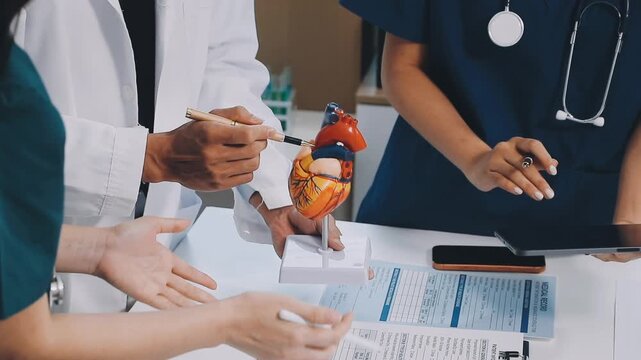 A vibrant red anatomical heart model and a stethoscope on a desk with two doctors having a medical consultation in the background.