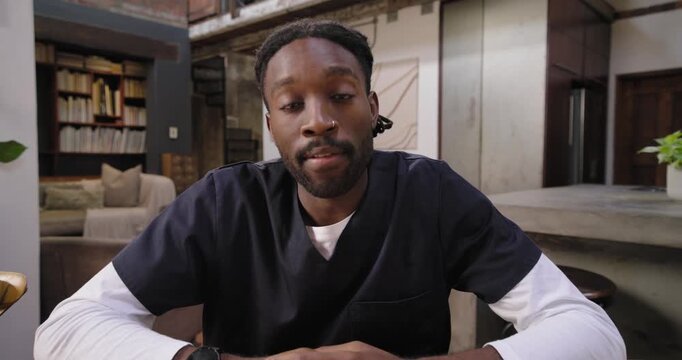 African male in scrubs leaning in, adjusting framing, settling and explaining on camera at table