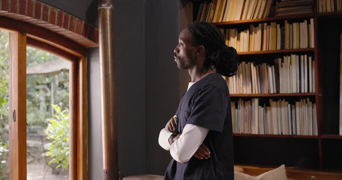 Adult African American male entering left in navy scrubs pausing at window in home library smiling
