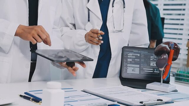 A vibrant red anatomical heart model and a stethoscope on a desk with two doctors having a medical consultation in the background.