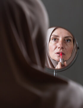 muslim woman applying make up in mirror wearing hijab