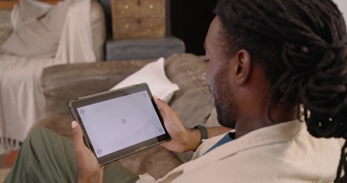 African American man in jacket holding tablet with corner marks aligning tablet on sofa, copy space