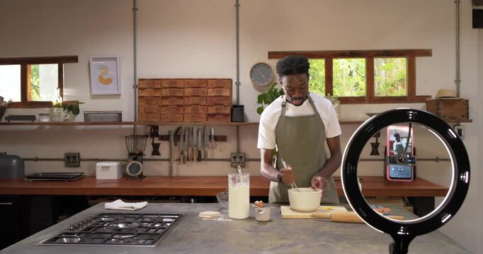 Phone recording, African American man in apron whisking in bowl at kitchen counter showing recipe