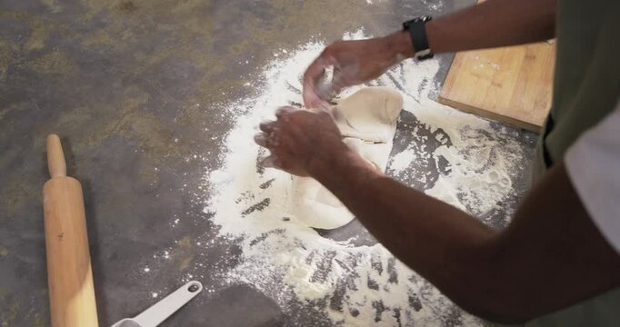 Spreading ring of flour, African man in green apron kneading dough for baking at kitchen counter