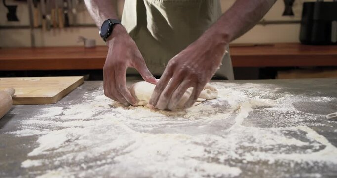 Man in green apron arranging pressing rolling kneading and shaping dough into loaf at metal counter