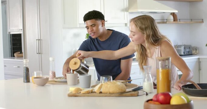 Couple, woman in tank top reaching across kitchen island, pouring French press coffee for breakfast