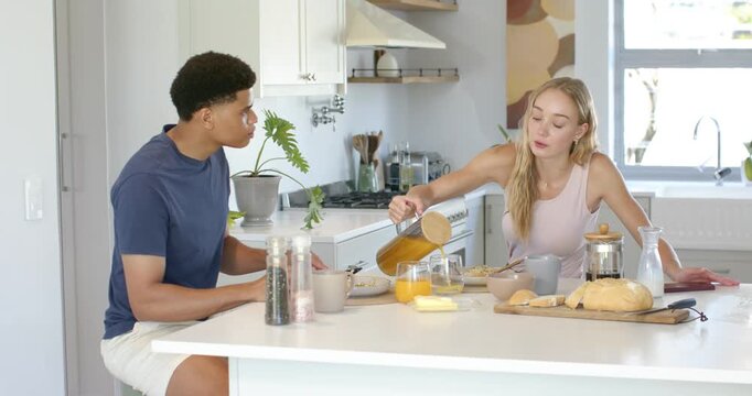 Couple sitting at kitchen island, woman reaching for pitcher and pouring orange juice for breakfast
