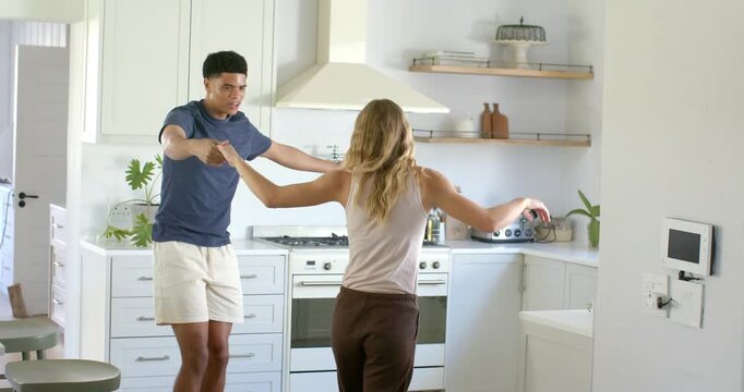 Couple holding hands, man lifting woman's hand and leading twirls for fun in bright kitchen stove