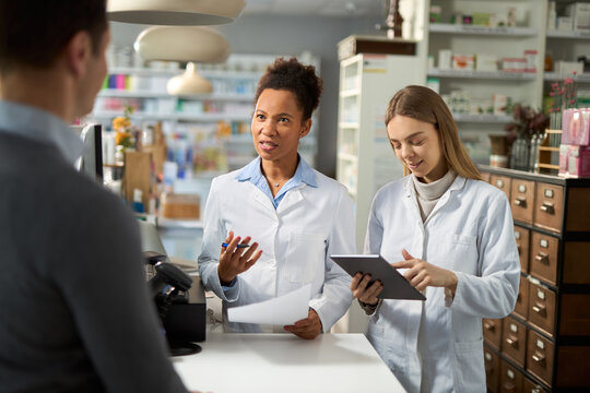 Happy female pharmacists using digital tablet while talking to a customer in a pharmacy