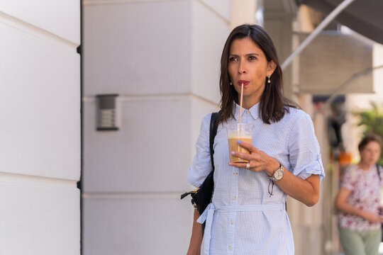 Businesswoman drinking iced coffee while walking in the city