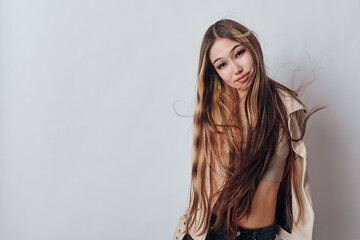 Fototapeta premium Young woman with long hair wearing casual clothes posing and smiling with head tilt on neutral background studio. Lifestyle, beauty, fashion and confidence with natural look.