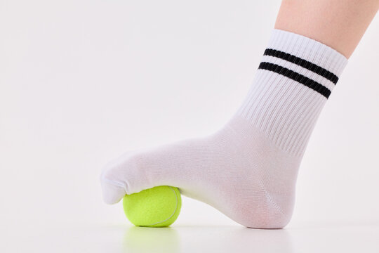 Foot in white sock pressing tennis ball for plantar fasciitis relief exercise