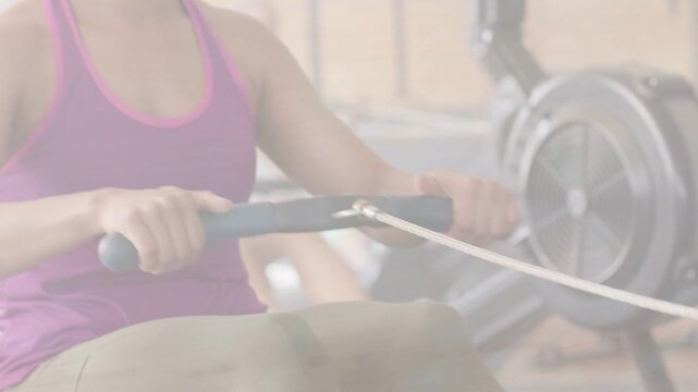 Vertical video: Gripping braided handle, woman in purple tank top rowing at gym class with flywheel