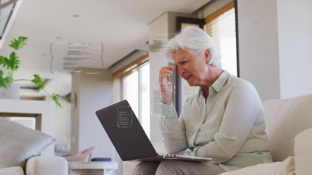 Senior woman leaning into laptop on sofa, UI overlays appearing, reading and understanding tech