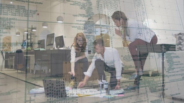 Three designers laying plans, using PC and adjusting model for design review, schematics overlaying