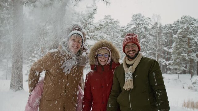 Portrait of positive company of four multiethnic gen Z friends posing for camera in winter forest, Black girl shaking snow off tree branch while boyfriend carrying her on his back