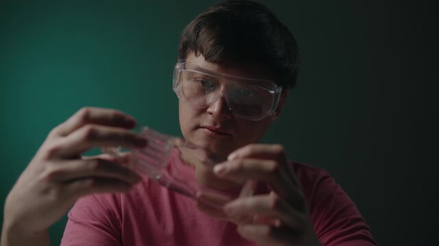 Portrait of artisan male in protective eyewear examining glass bottle, preparation to transforming waste into new handcrafted object in creative diy workshop session. Shooting in slow motion.