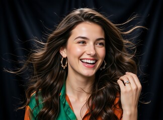 Fototapeta premium Young woman with long wavy brown hair laughing in studio. Happy female model with gold hoop earrings on dark background. Joyful expression and dental health concept
