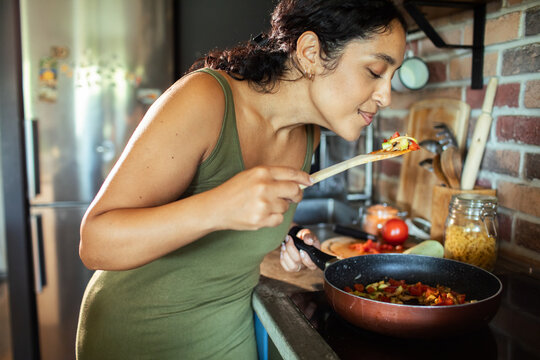 Pregnant woman tasting vegetables while cooking at home kitchen