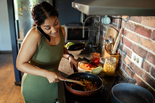 Woman cooking and talking on phone in home kitchen