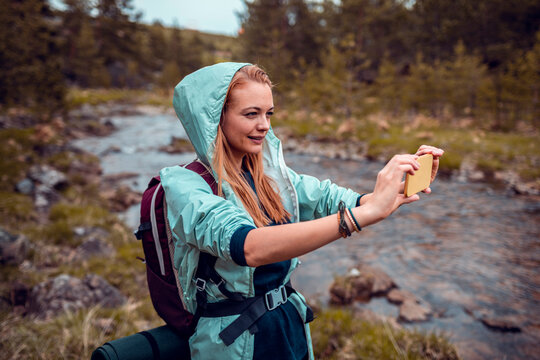 Young woman hiker taking smartphone photo by mountain river