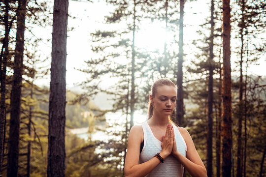 Young woman meditating with prayer hands in forest