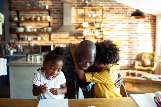 Smiling father hugs children in home kitchen