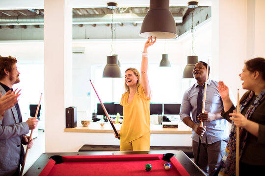 Happy coworkers playing pool in modern office break area