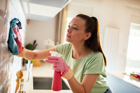 Woman cleaning kitchen tiles at home with spray bottle