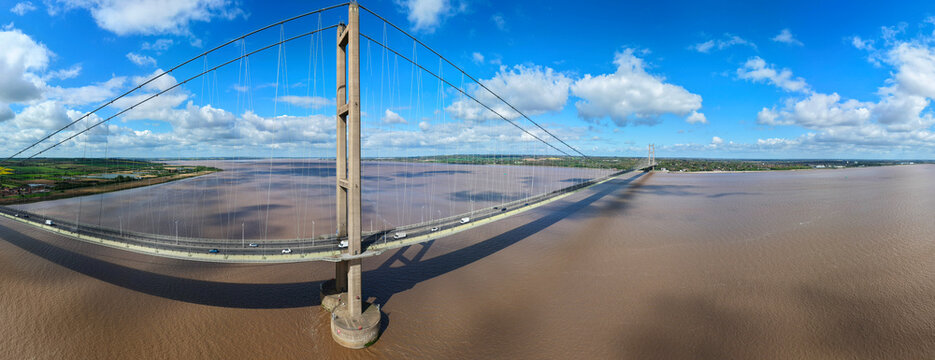 Aerial view of the Humber Bridge suspension structure spanning the wide estuary with traffic and fluffy clouds Kingston upon Hull, England, United Kingdom.