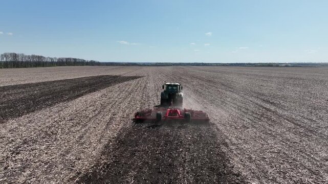 modern tractor working with disc harrow on the field with corn residue