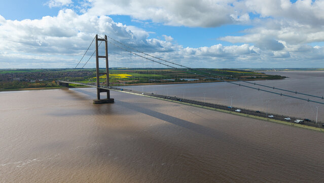 Aerial view of the Humber Bridge spanning the estuary with traffic and green fields under a cloudy sky Kingston upon Hull, England, United Kingdom.