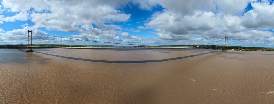 Aerial view of the Humber Bridge suspension bridge spanning the Humber Estuary under a cloudy blue sky in Kingston upon Hull, England, United Kingdom.