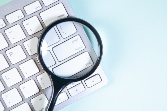 Magnifying glass and computer keyboard on blue background. Top view.