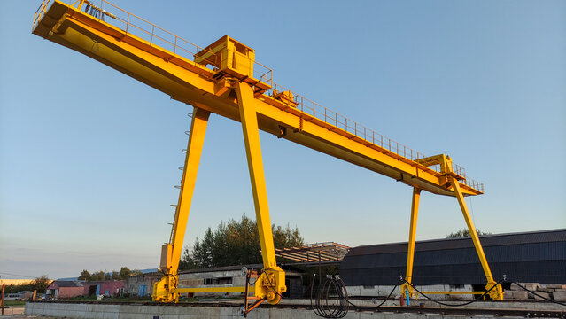 A massive yellow gantry crane stands over an industrial railway yard under a clear blue sky. Heavy logistics operation, freight transportation, industrial infrastructure.