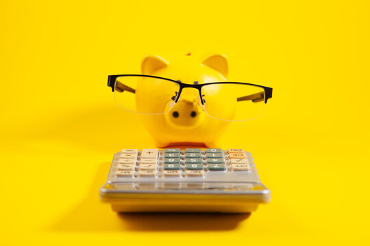 Piggy bank with glasses and calculator on bright yellow background.