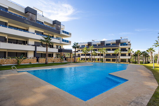 Modern apartment complex with large swimming pool, sun terrace and palm trees in luxury residential development