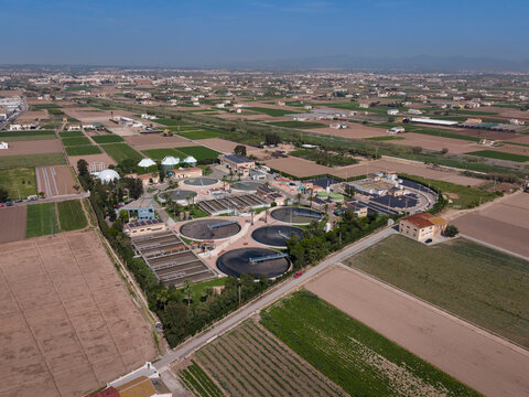 Aerial view of wastewater treatment plant showing circular sedimentation tanks, aeration basins, primary settling basins, anaerobic digesters with biogas domes, and biological treatment units surround