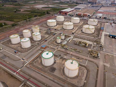 Top-down view of a fuel storage terminal with large white oil tanks, green roofs, pipeline network, pump stations and containment berms in an industrial facility