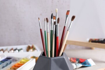 Fototapeta premium Paintbrushes in holder and paints on light table, closeup