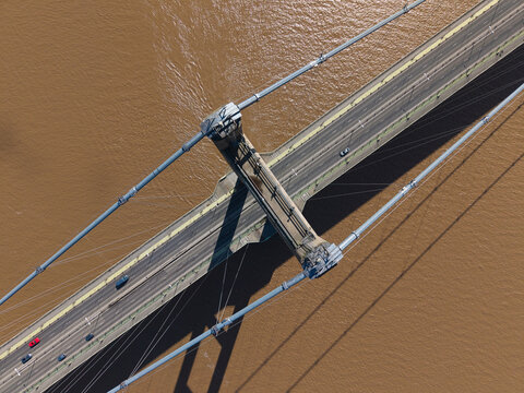 Aerial view of the Humber Bridge showing suspension cables and cars driving on the roadway over the brown water of the estuary in Kingston upon Hull, England, United Kingdom.