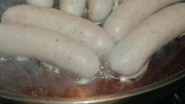 White German sausages simmering in dark beer in a pan
