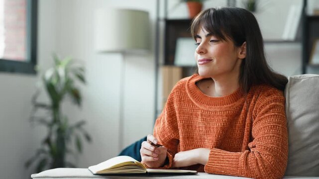 Video of beautiful writer taking notes in a notebook while sitting on the couch at home