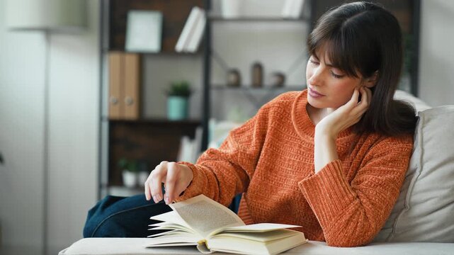 Video of pretty woman reading a book while sitting on the couch at home