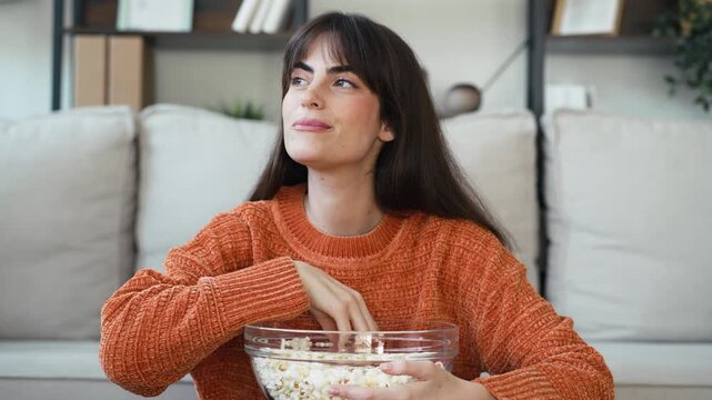 Video of happy woman eating popcorn while sitting on the sofa in the living room at home